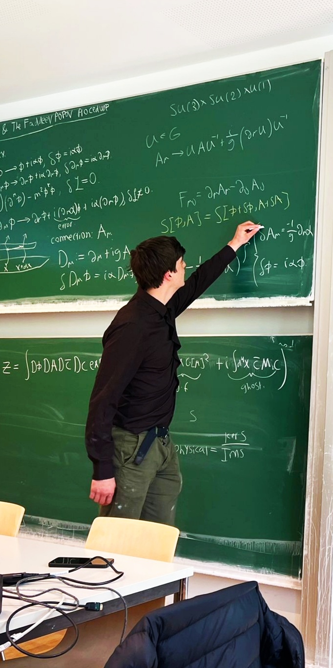Noah writing gauge theory equations on a chalkboard